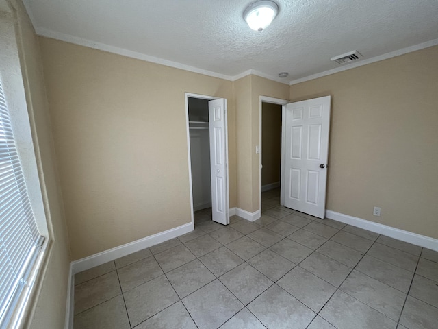 unfurnished bedroom with light tile patterned flooring, ornamental molding, a textured ceiling, and a closet