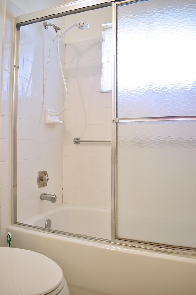 bathroom featuring toilet and bath / shower combo with glass door