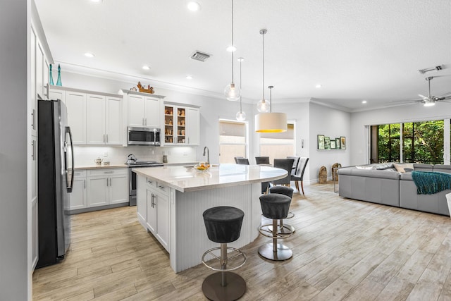 kitchen featuring white cabinetry, pendant lighting, a breakfast bar, a center island with sink, and appliances with stainless steel finishes