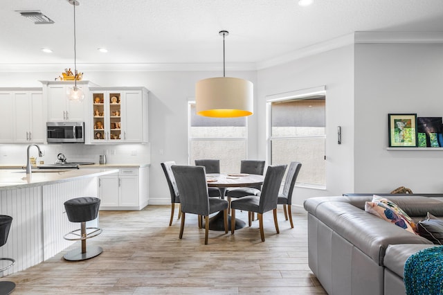 dining room featuring crown molding, light hardwood / wood-style flooring, a textured ceiling, and sink