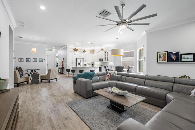 living room featuring a textured ceiling, light hardwood / wood-style floors, ceiling fan, and crown molding