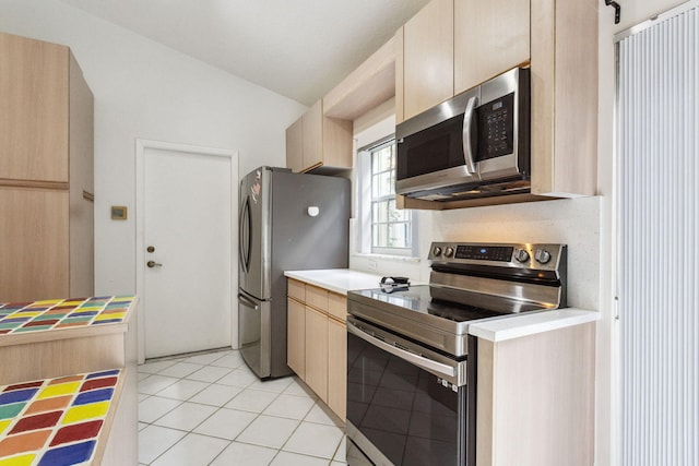 kitchen featuring lofted ceiling, light brown cabinets, light tile patterned floors, and stainless steel appliances