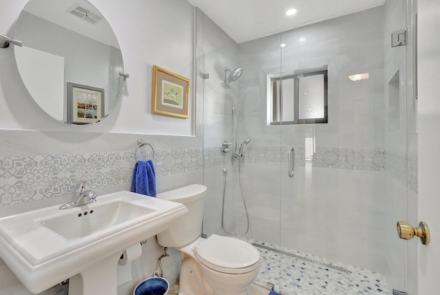 bathroom with sink, a shower with shower door, tile walls, and toilet