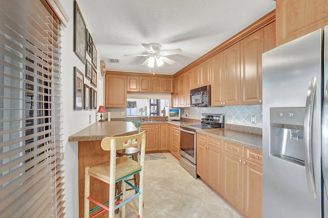 kitchen with ceiling fan, a breakfast bar, stainless steel appliances, and a textured ceiling