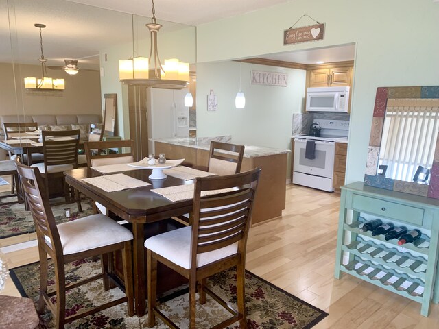 dining room with ceiling fan with notable chandelier and light hardwood / wood-style floors