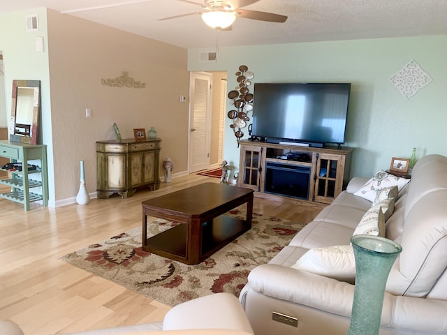 living room with ceiling fan, wood-type flooring, and a textured ceiling