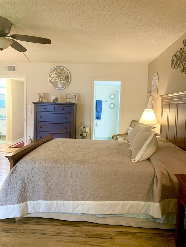 bedroom featuring ceiling fan, ensuite bathroom, wood-type flooring, and a textured ceiling