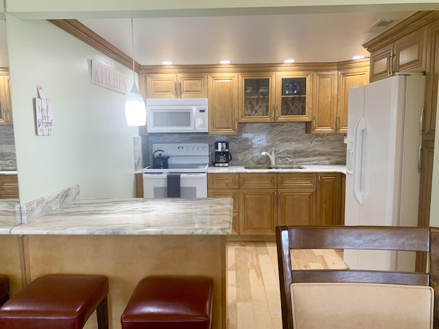 kitchen with white appliances, sink, pendant lighting, light hardwood / wood-style flooring, and a breakfast bar area