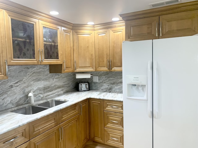 kitchen featuring decorative backsplash, white fridge with ice dispenser, light stone counters, and sink