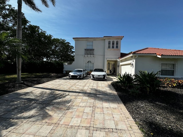 mediterranean / spanish home with decorative driveway, a tiled roof, an attached garage, and stucco siding