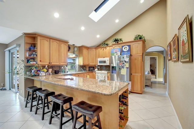 kitchen with a skylight, high vaulted ceiling, kitchen peninsula, white appliances, and a kitchen bar