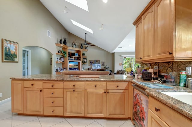 kitchen with kitchen peninsula, light brown cabinetry, a skylight, light tile patterned floors, and high vaulted ceiling