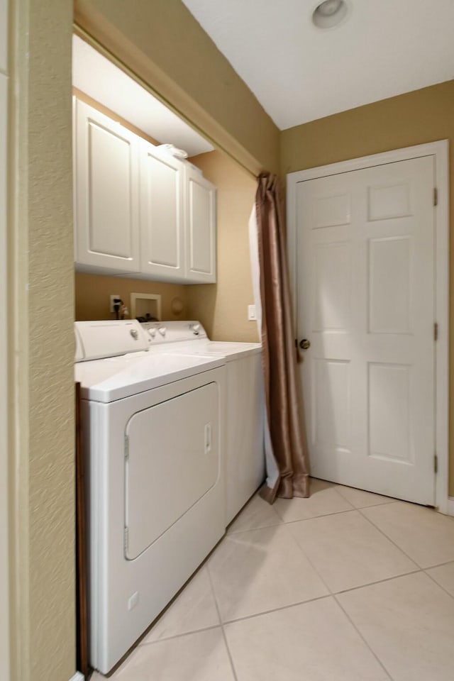 laundry area with washer and clothes dryer, light tile patterned flooring, and cabinets