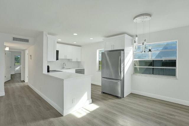 kitchen featuring stainless steel appliances, sink, light hardwood / wood-style flooring, white cabinetry, and hanging light fixtures