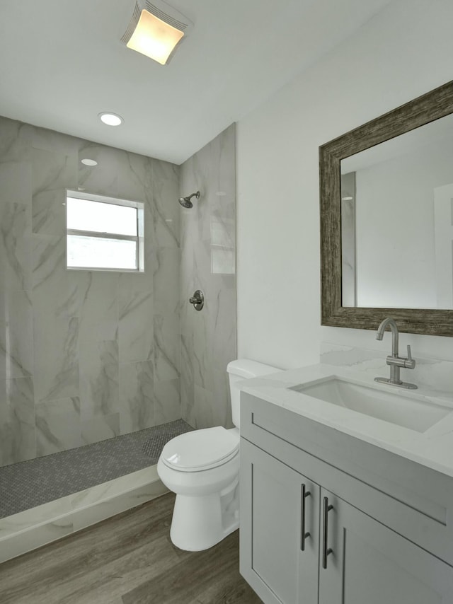 bathroom with tiled shower, hardwood / wood-style floors, vanity, and toilet