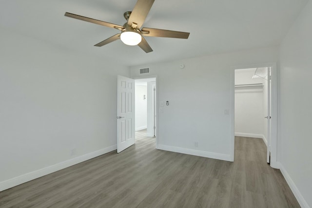 unfurnished bedroom with ceiling fan, light hardwood / wood-style floors, a walk in closet, and a closet