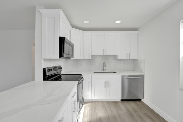 kitchen with sink, decorative backsplash, light wood-type flooring, appliances with stainless steel finishes, and white cabinetry