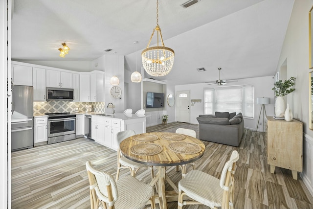 dining space featuring ceiling fan with notable chandelier, light hardwood / wood-style floors, lofted ceiling, and sink