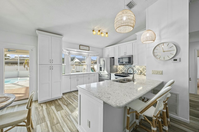 kitchen with kitchen peninsula, appliances with stainless steel finishes, a kitchen breakfast bar, vaulted ceiling, and white cabinets