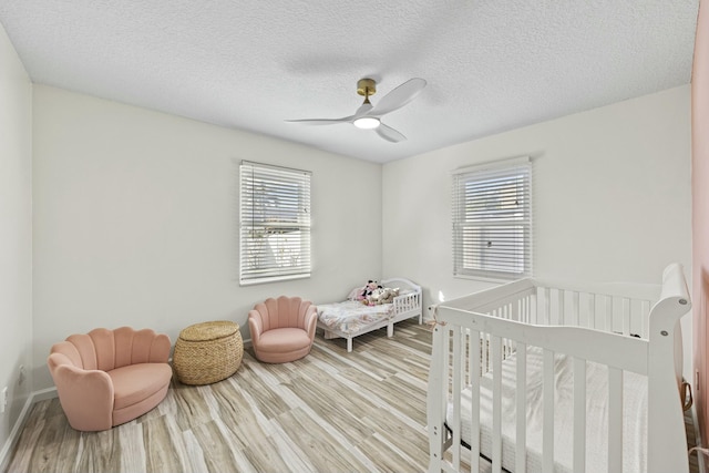 bedroom featuring ceiling fan, a nursery area, a textured ceiling, and light wood-type flooring