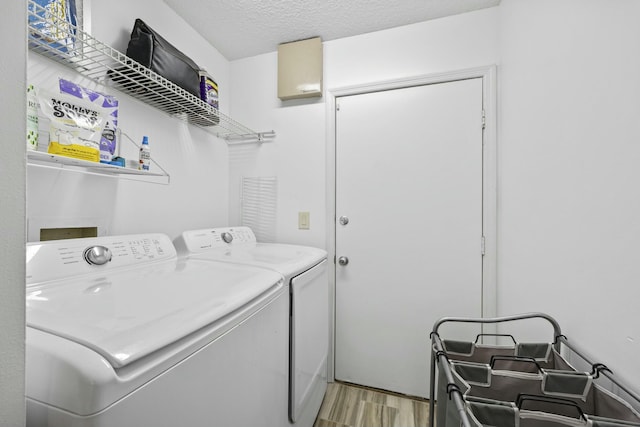 laundry room featuring a textured ceiling, separate washer and dryer, and light hardwood / wood-style flooring