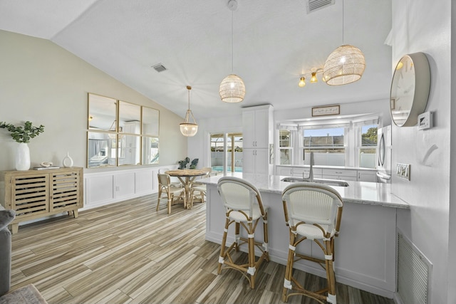 dining area with vaulted ceiling, sink, and light hardwood / wood-style flooring