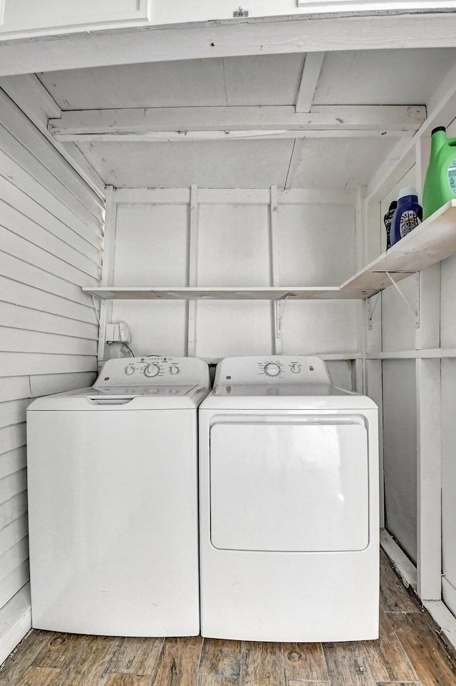 clothes washing area featuring separate washer and dryer, dark hardwood / wood-style floors, and wooden walls