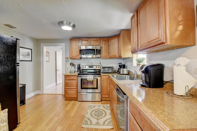 kitchen with light wood-type flooring, stainless steel appliances, tasteful backsplash, and sink