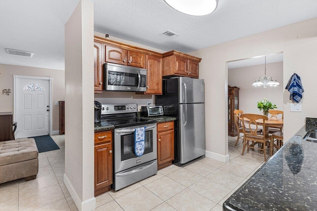 kitchen with a textured ceiling, light tile patterned floors, a notable chandelier, pendant lighting, and stainless steel appliances