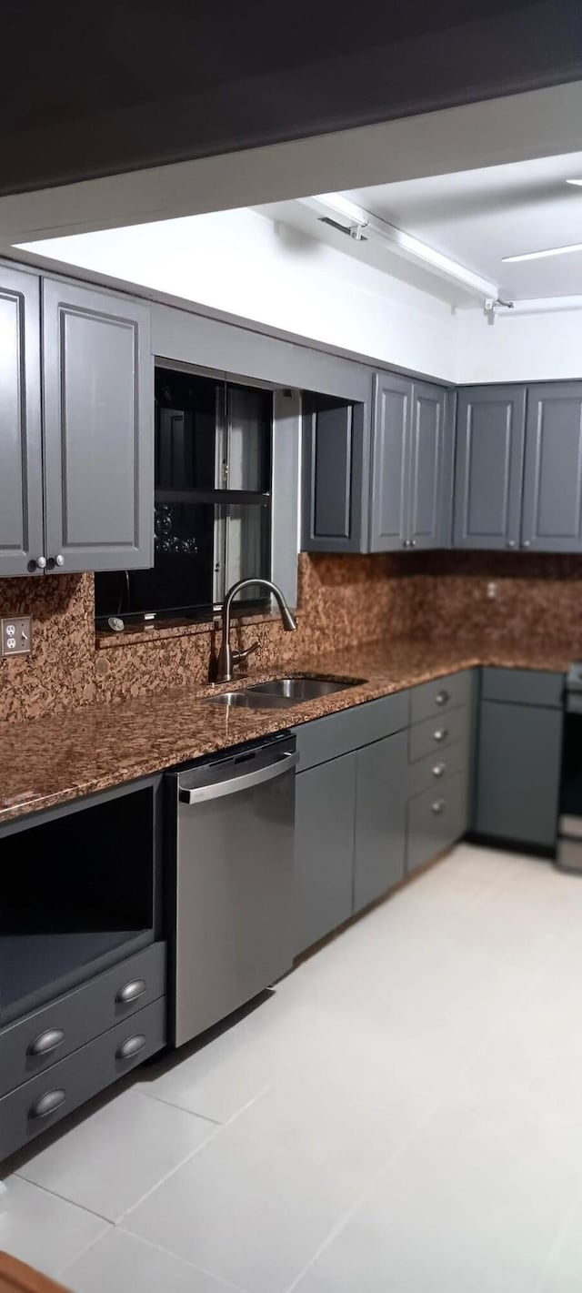 kitchen with dark stone counters, decorative backsplash, gray cabinets, stainless steel dishwasher, and a sink