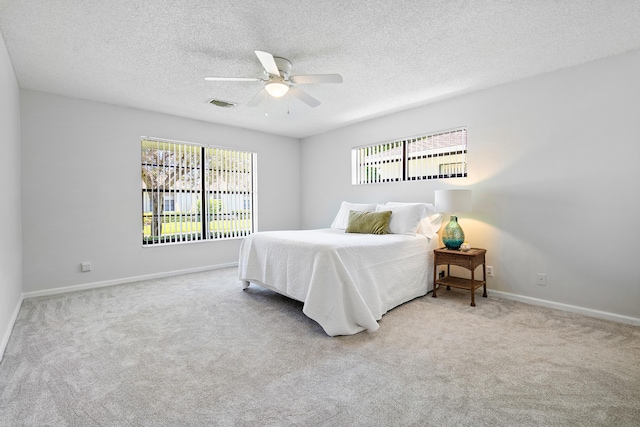 bedroom featuring a textured ceiling, ceiling fan, light carpet, and multiple windows