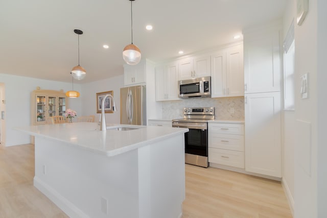 kitchen featuring a center island with sink, appliances with stainless steel finishes, white cabinets, and hanging light fixtures