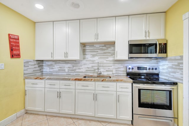 kitchen with appliances with stainless steel finishes, backsplash, sink, white cabinetry, and light tile patterned flooring