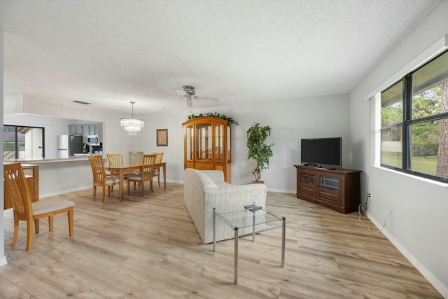 living room featuring ceiling fan with notable chandelier, light wood-type flooring, and a textured ceiling