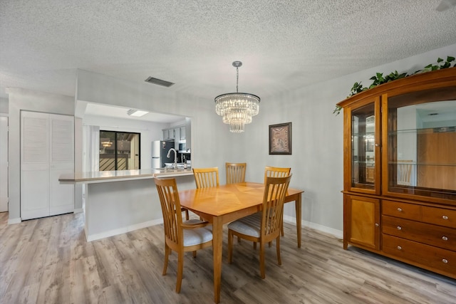 dining space with a chandelier, a textured ceiling, and light hardwood / wood-style flooring