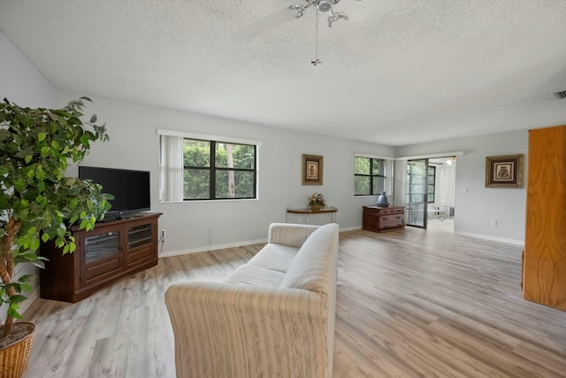 living room with a textured ceiling, light wood-type flooring, a wealth of natural light, and ceiling fan