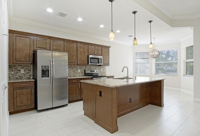 kitchen featuring a kitchen island with sink, hanging light fixtures, sink, crown molding, and stainless steel appliances