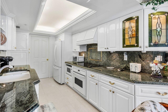 kitchen with decorative backsplash, white appliances, a tray ceiling, light tile patterned floors, and white cabinetry