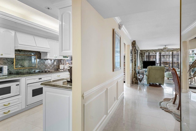 kitchen with premium range hood, dark stone counters, white appliances, ceiling fan, and white cabinetry