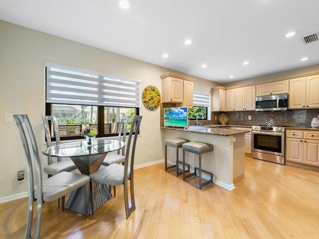 kitchen with a kitchen breakfast bar, dark stone countertops, a wealth of natural light, and appliances with stainless steel finishes