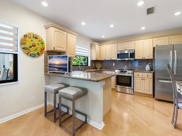 kitchen featuring sink, a breakfast bar area, dark stone countertops, light wood-type flooring, and stainless steel appliances