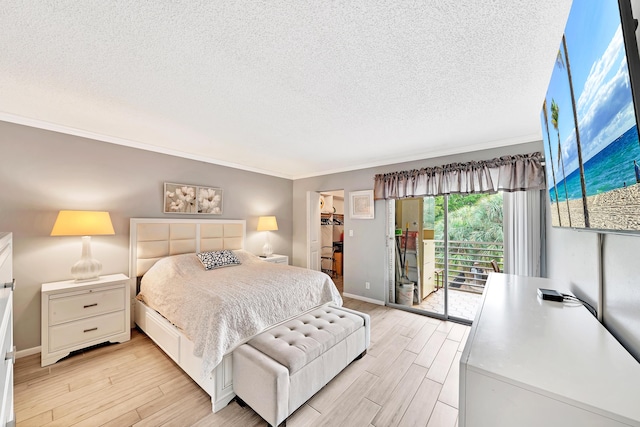 bedroom with light wood-type flooring, a textured ceiling, access to outside, a walk in closet, and ornamental molding