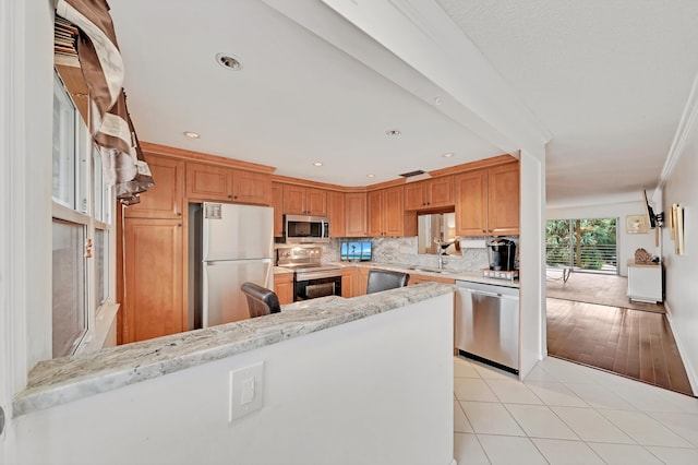 kitchen featuring light stone countertops, backsplash, light wood-type flooring, appliances with stainless steel finishes, and ornamental molding