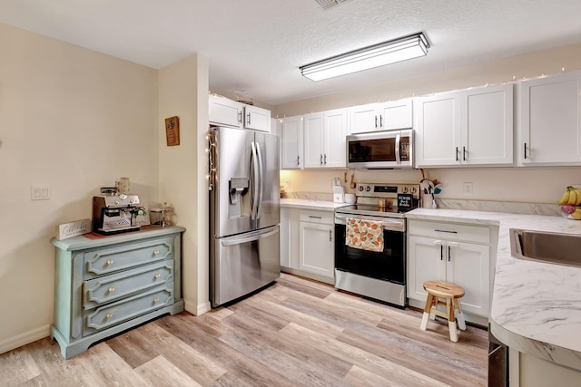 kitchen with appliances with stainless steel finishes, light wood-type flooring, a textured ceiling, sink, and white cabinets