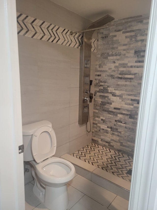 bathroom with tile patterned floors, toilet, tiled shower, and tile walls