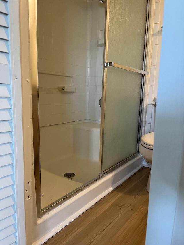 bathroom with toilet, wood-type flooring, and a shower with door