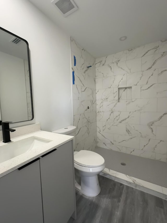 bathroom with vanity, hardwood / wood-style floors, toilet, and tiled shower