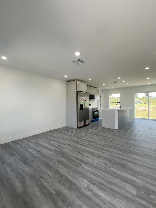 kitchen with sink, stainless steel appliances, dark hardwood / wood-style flooring, and an island with sink