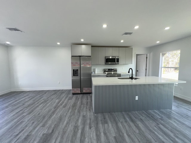 kitchen with appliances with stainless steel finishes, an island with sink, wood-type flooring, sink, and gray cabinetry