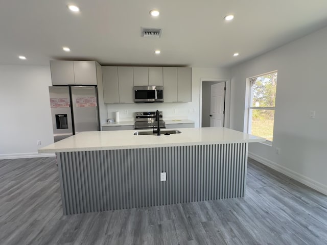 kitchen with sink, gray cabinetry, light hardwood / wood-style flooring, a center island with sink, and stainless steel appliances